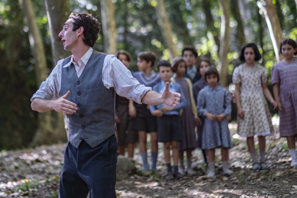 Still from the movie. The teacher dances while his students watch him. They are in a forrest.